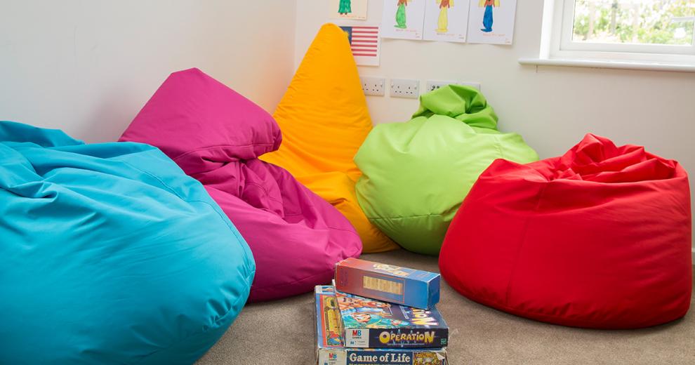 Comfortable, plush, multicoloured, vibrant bean bag seating area within easy reach of a stack of games.