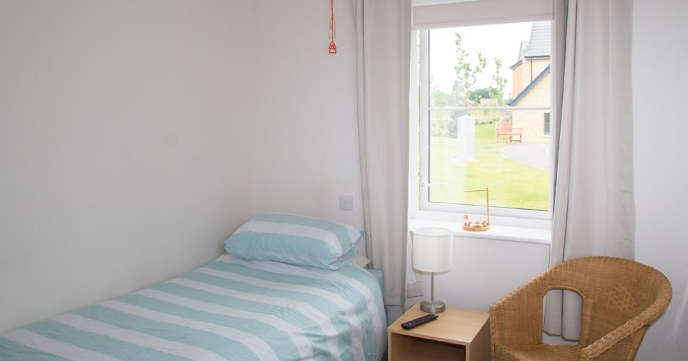 Tranquil cosy bedroom with bed, wicker chair and views out to the grassed seating area.