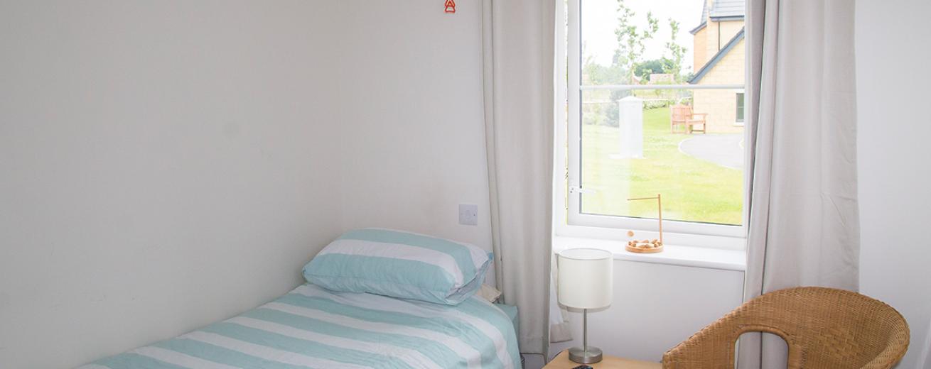 Tranquil cosy bedroom with bed, wicker chair and views out to the grassed seating area.