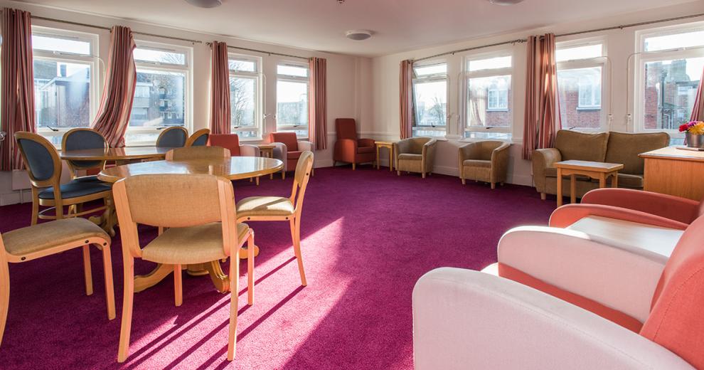 Bold pink seating area, with a fuchsia carpet throughout with becomes more vibrant from the mass amounts of natural light from the windows filling the two walls. Multiple soft seating options are available from salmon and light pink arm chairs, grey crushed armchairs and two seater sofa, as well as multiple circular tables with matching cream upholstered chairs.