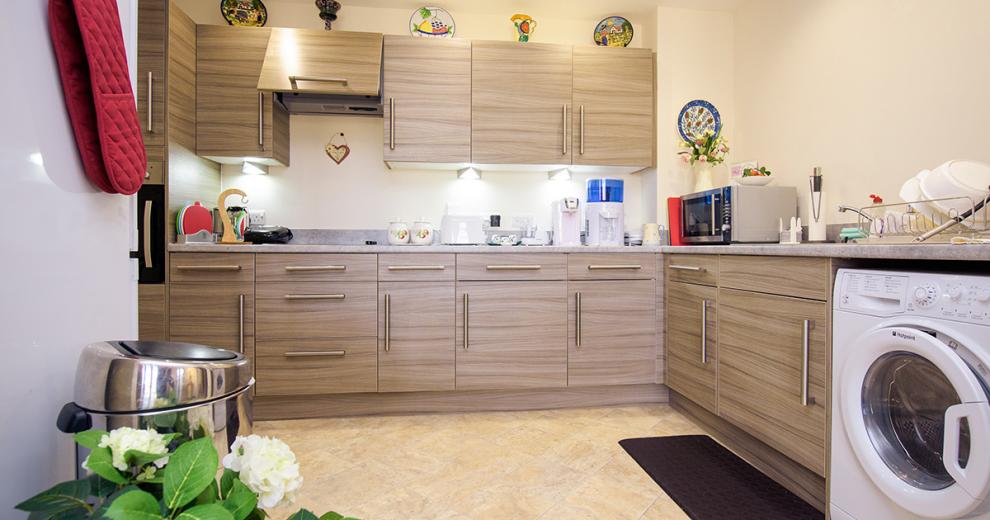 A spacious, effortlessly modern kitchen area designed in earth toned cabinetry, the grey mottled worktop adds a fresh look to the room. The kitchen houses a washing machine, microwave, electric hob and wall mounted oven.