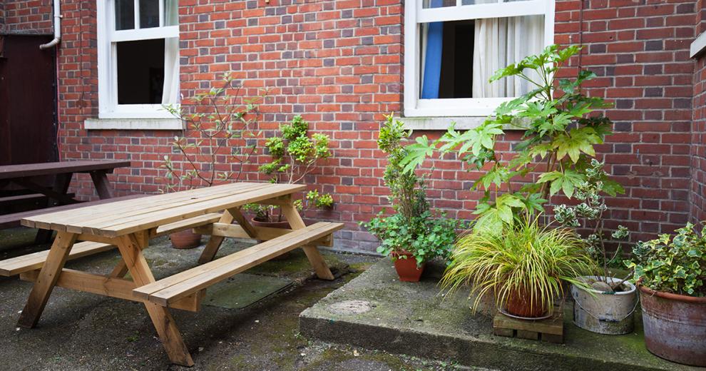 Multiple bench seating on a concrete outdoor area, next to an array of potted plants on a raised concrete platform.