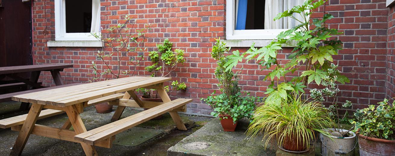 Multiple bench seating on a concrete outdoor area, next to an array of potted plants on a raised concrete platform.