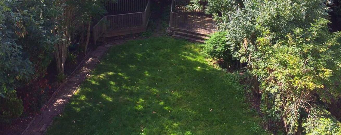 Maintained, minimal garden with pathway leading the whole length. With two raised wooden patios shaded by mature trees and a large grass area.