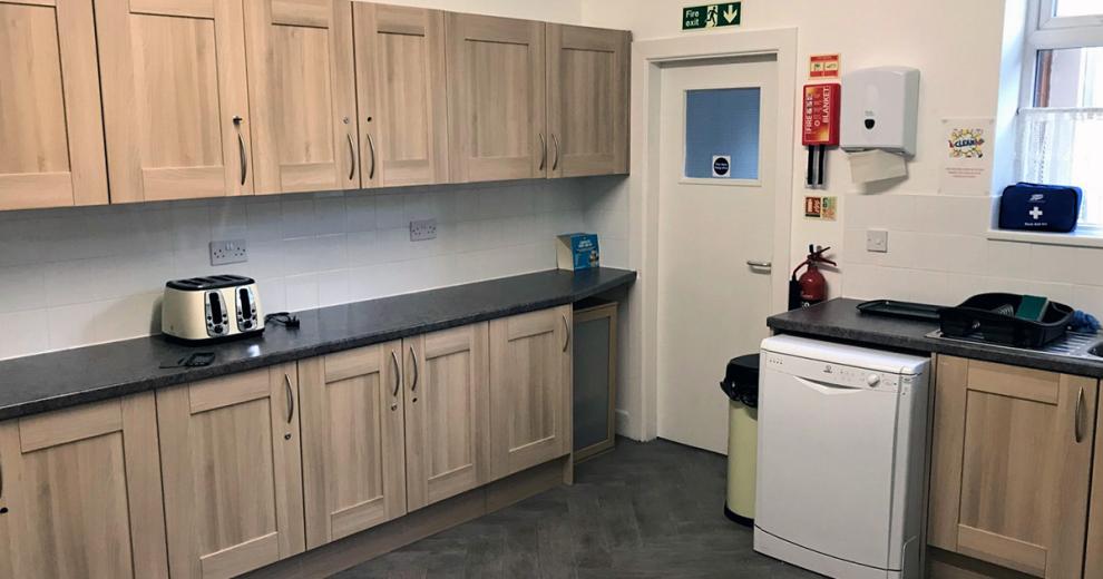Abundant amount of mid-brown stained oak kitchen cabinets, with speckled black worktop and white goods appliances.