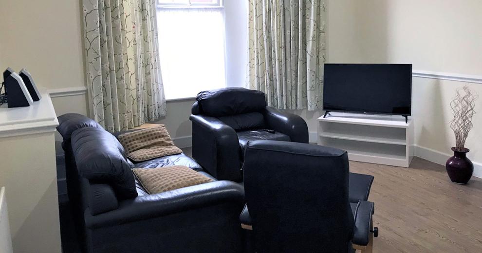 Large simplistic, calming living area, featuring numerous seating options facing into a good sized television.