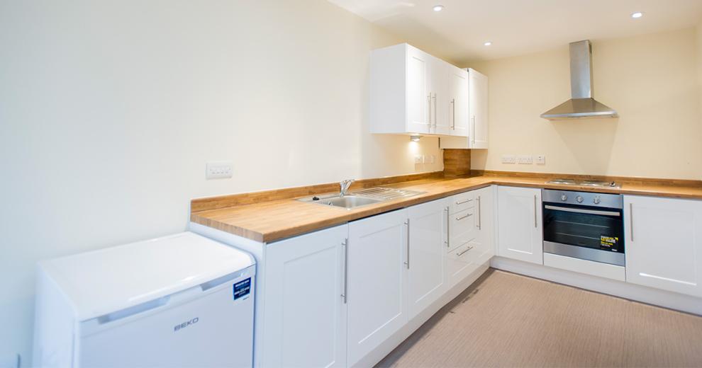 Stylized contemporary kitchen with all modern appliances and thick wooden work surface. As well as illuminating spotlights in the ceiling.