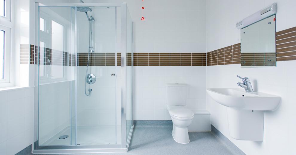 An immaculate brilliant white shower room with stylish brown tiled stripe creating a central boarder to the room. Featuring an oversized shower with waterfall head and white toilet and wall mounted sink.