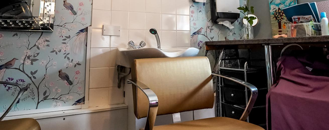 A charming in-house hair salon, with a delicate pastel, bird patterned feature wall. Amongst the multiple salon chairs, wall mounted hair washing sink, hair dressing trolley and extended worktop along the wall.