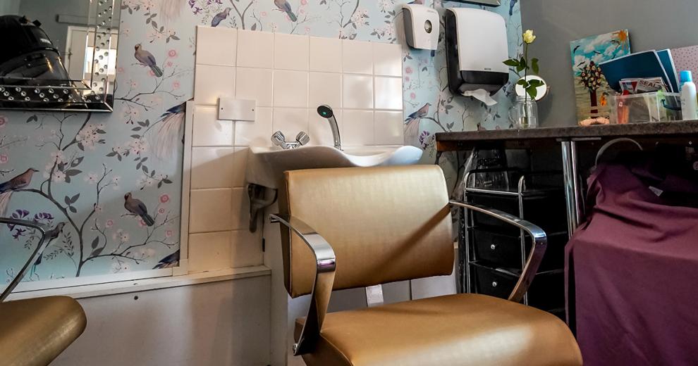 A charming in-house hair salon, with a delicate pastel, bird patterned feature wall. Amongst the multiple salon chairs, wall mounted hair washing sink, hair dressing trolley and extended worktop along the wall.