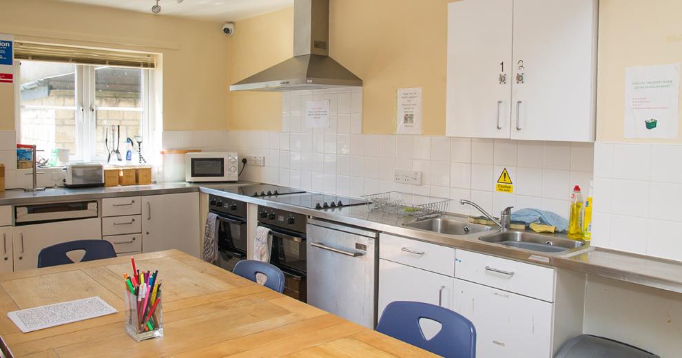 Sunny pastel yellow food preparation area. Hosting two ovens, two ceramic hobs, dishwasher and double fitted sink. As well as communal eating area in the centre of the room.