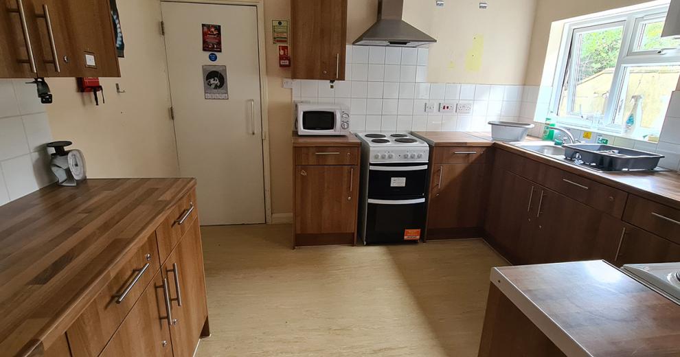 Chestnut brown kitchen counter with identical kitchen cupboard units, fitted with white goods and window views out into the garden.