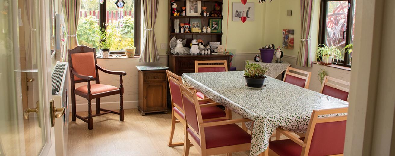 Homely, dining room area with bulky wooden furniture, red upholstered dining chairs and patterned tablecloth.
