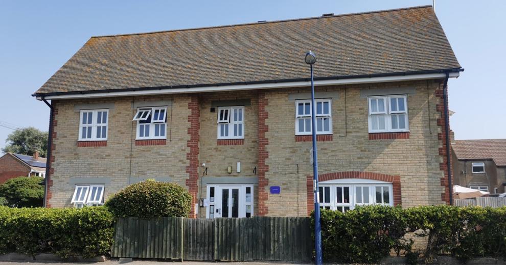 Weathered brick, cottage style two storey property. Waist height fencing filling in-between the hedges around the perimeter.