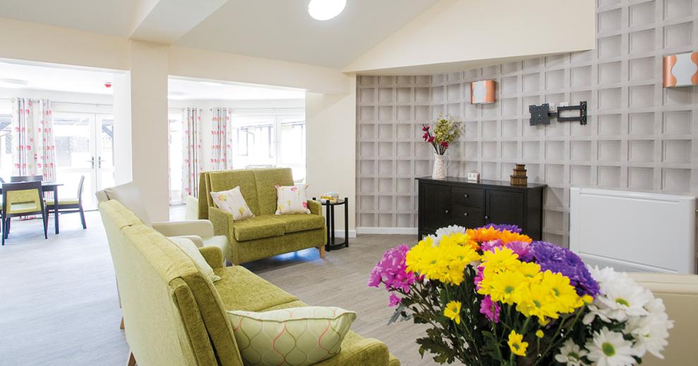 The wood panelled wallpaper feature wall creates a stylish television area, with wall mounted lighting large ark wooden unit and bright floral displays.