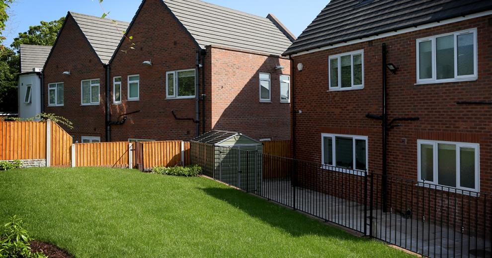 The slab paving walkway around the property includes a secure wooden shed and access to a sloped elevated garden which has been secured by a black metal fence.