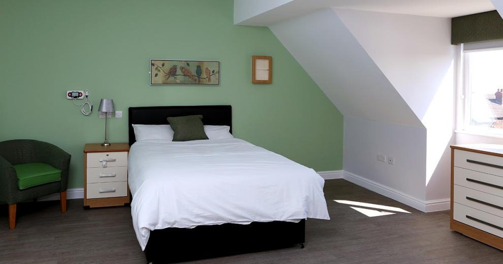 Simply designed pale green and white bedroom with complimentary bird artwork, soft wooden furniture accessories and a double bed.