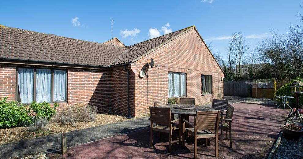 A designated patio area to the side of the property is home to a large six-person wooden outdoor table and chairs.