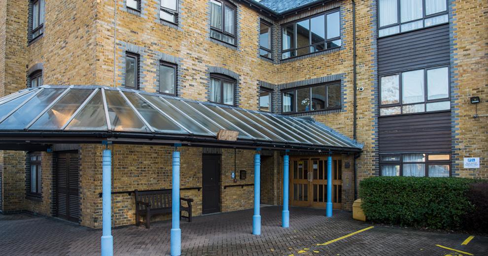 A sheltered roof is supported by blue columns and attached to the perimeter allowing cover for anyone using the entrance to the property.