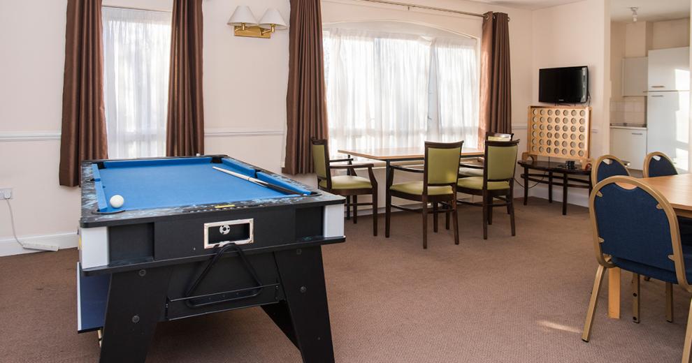 A good sized room with a blue speckled snooker table located at the top of the room, two four person dining sets are placed the other end linking into the kitchenette.