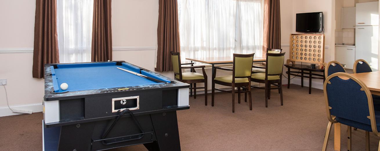A good sized room with a blue speckled snooker table located at the top of the room, two four person dining sets are placed the other end linking into the kitchenette.