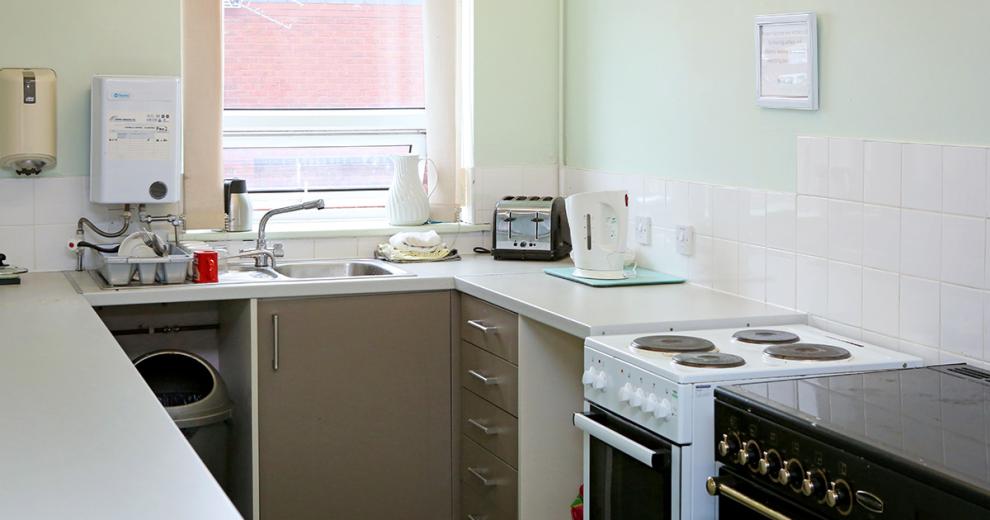 Clean and compact galley styled kitchen, using pastel mint paint to blend into the squared white tiles. The appliances are mix and matched having one blank and gold oven and hob as well as a white and black oven and hob, silver bin, white kettle and silver and black toaster.