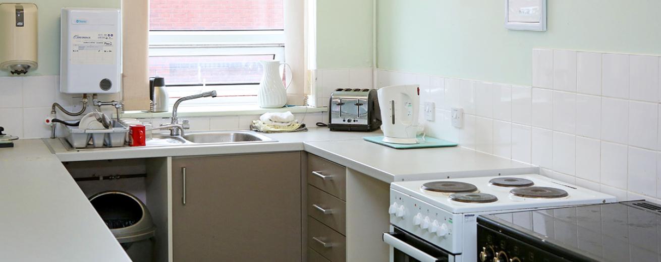 Clean and compact galley styled kitchen, using pastel mint paint to blend into the squared white tiles. The appliances are mix and matched having one blank and gold oven and hob as well as a white and black oven and hob, silver bin, white kettle and silver and black toaster.