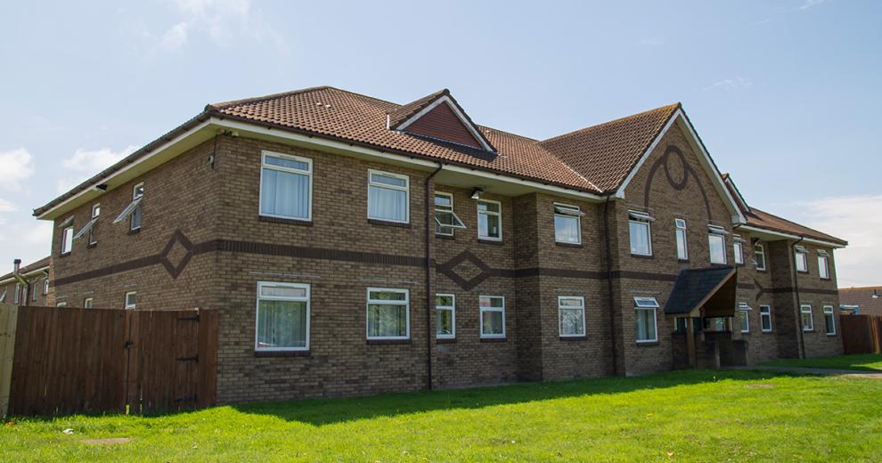 Substantial sized property featuring built-in brick design, sectioned off with wooden fencing and a central paved walkway between the grass areas leading to the entrance.