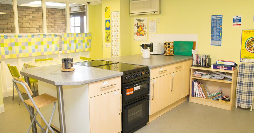 The large bold yellow kitchen hosts a stand alone wall adjoined central island which has two back to back oven and hobs and cabinets spalling the rest of the counter space. Tucked into the alcove of the room hosts a four-person dining table with lime green seating to contrast with the yellow décor.