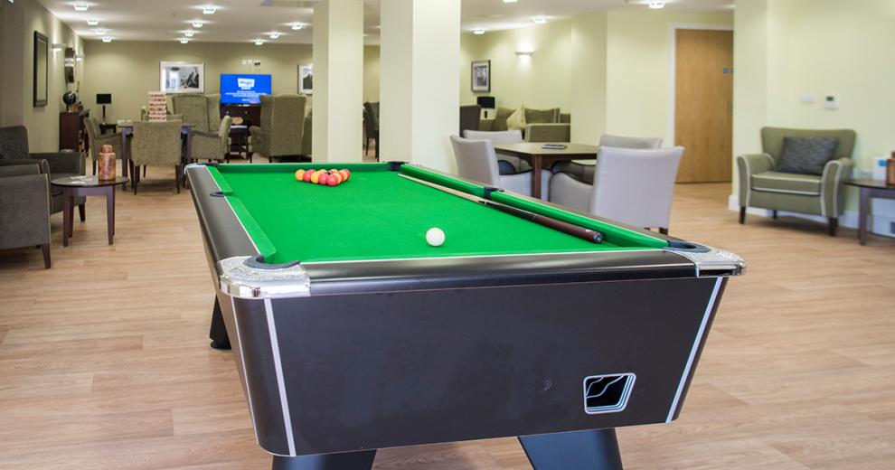 At the back of the seating area a professional sized, dark wood with silver trimming and green quilted pool table with plenty of space.