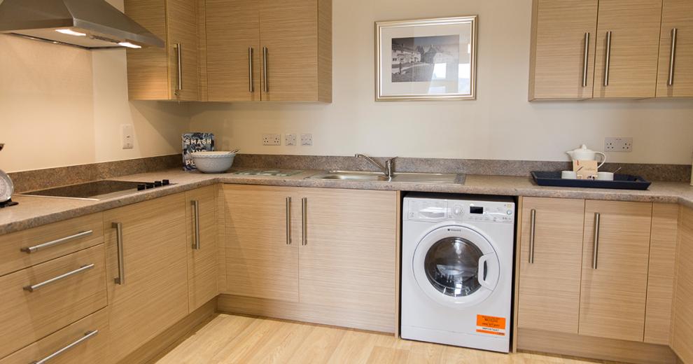 Gorgeous wood panelled kitchen cabinets a slightly lighter wooden flooring, finished with a soft marble effect worktop, white goods, and an integrated hob.