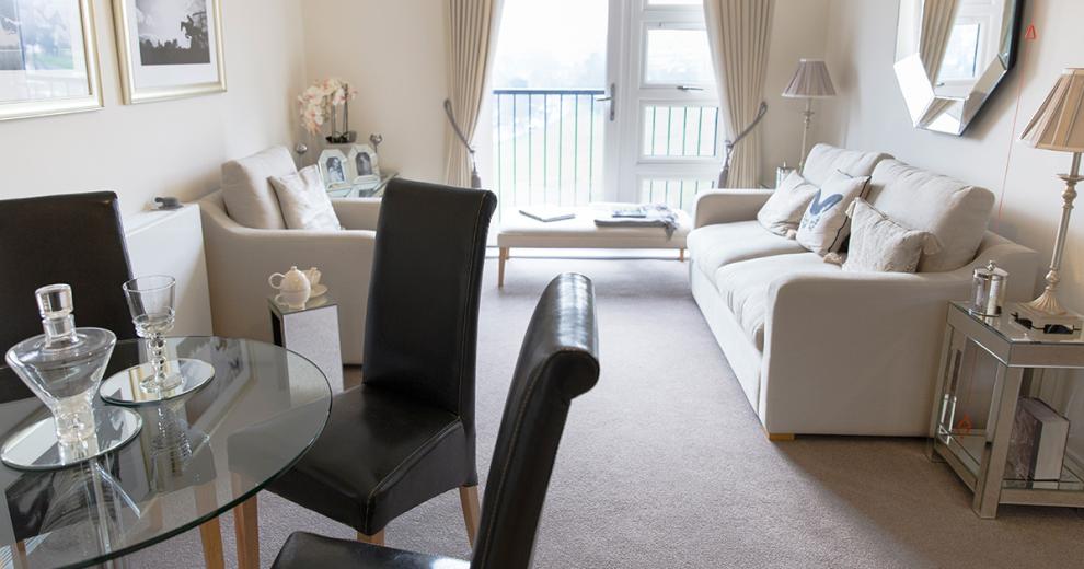 A tastefully decorated open plan living dining area with cream furnishings, there is a patio door which leads to a Juliet balcony which is letting in natural light