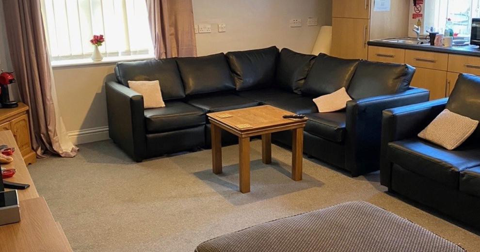 Relaxed, modern seating area home to a large black leather corner suite and matching black leather armchair. Decorated with cream cushions, and a small square coffee table.