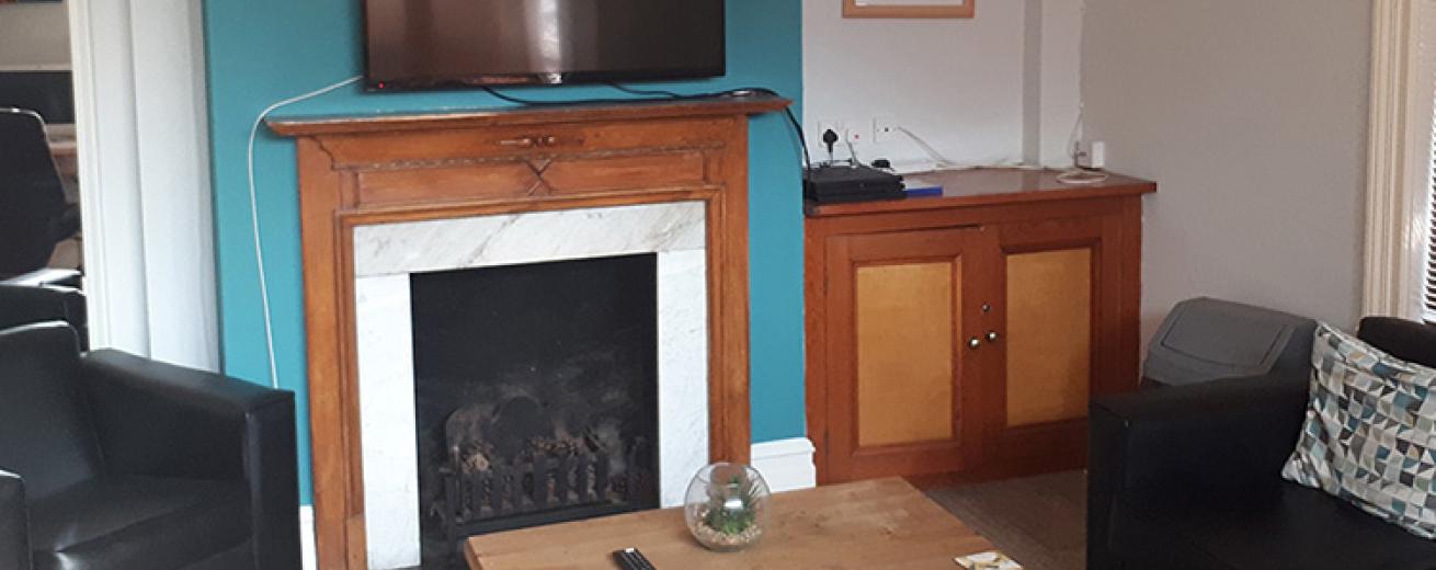 Wall mounted television with a selection of black leather seating. Located in an intimate, teal and white room.