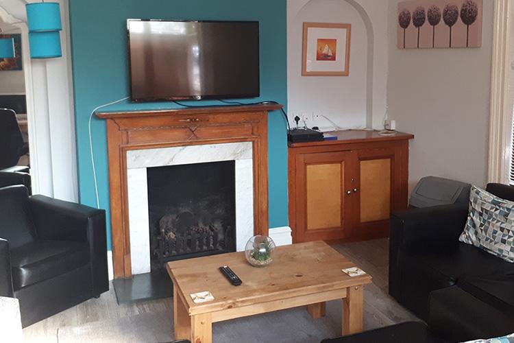 Wall mounted television with a selection of black leather seating. Located in an intimate, teal and white room.