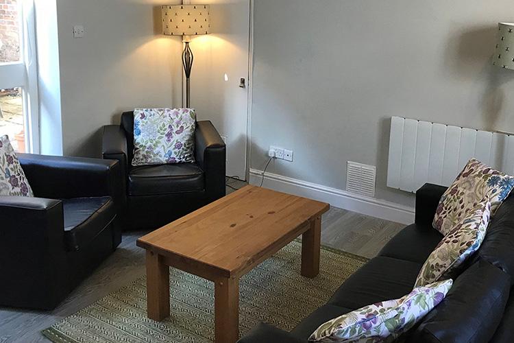 Relaxed, modern seating area consisting of a three-person black sofa with two matching match armchairs. Accessorised with twin floor lamps, decorative cushions, and a coffee table.