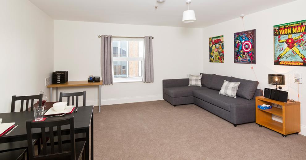 Uncrowded, neutral toned seating area. Grey corner suite sofa with plush cushions. A four-person dining table, set for a meal.