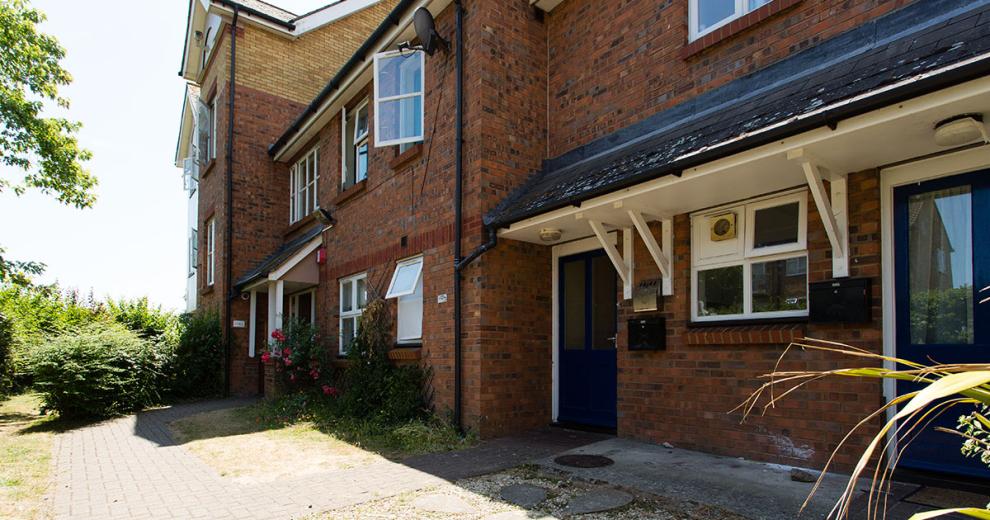 Detached, two storey supported housing property. With scattered windows and centralised blue door and porch.