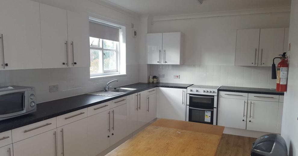 Garden facing window allowing natural light into a brilliant white kitchen, fitted with plenty of storage and workplace space. The white and silver colour scheme are followed through to the household appliances.