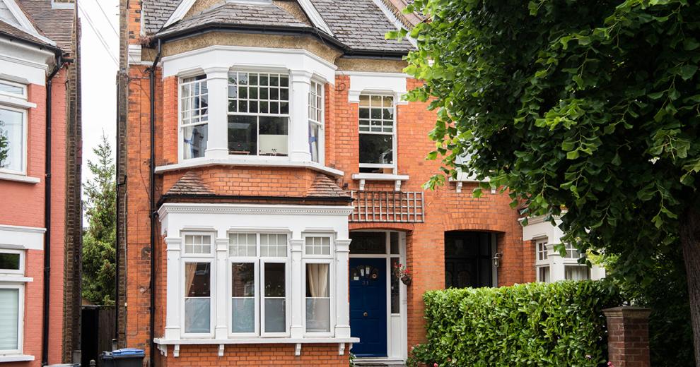Grandiose white bay windows with checked design. Navy blue doorway and privacy provided by a well-kept hedge. As well as a thin walkway to gain access to the back of the property.