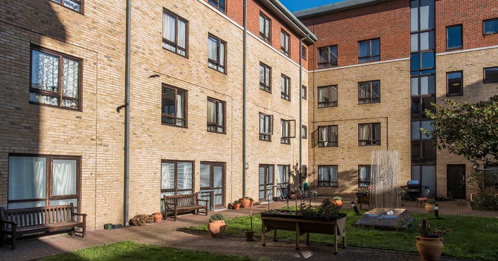 The garden is neatly divided into sections. The multiple wooden benches frame the perimeter of the outdoor area, looking in onto a raised potting station, neatly kept grass and walkways lined with terracotta pots and beautiful flowers.