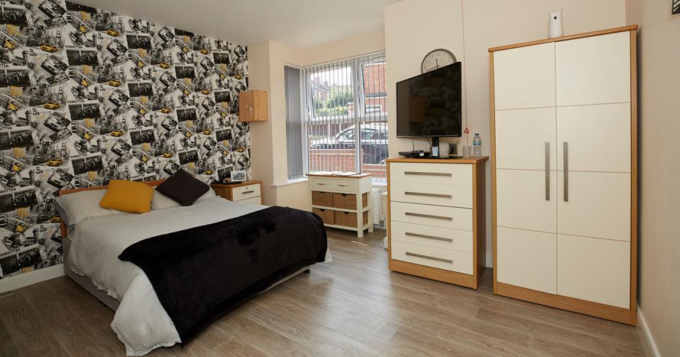 Contemporary. roomy double bedroom with feature wall, plenty of light-coloured storage and large windows allowing light and views out to a communal car park.
