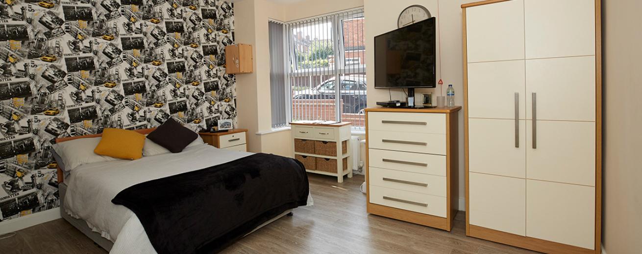 Contemporary. roomy double bedroom with feature wall, plenty of light-coloured storage and large windows allowing light and views out to a communal car park.