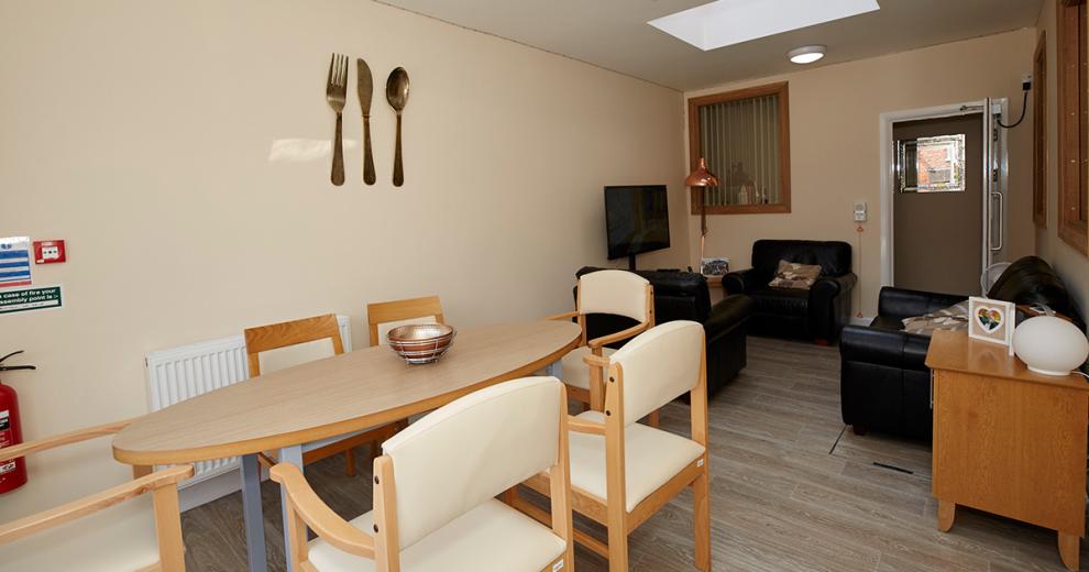 Kitchen utensil wall art behind an oval dining table with six-person seating flowing through to the communal seating area.