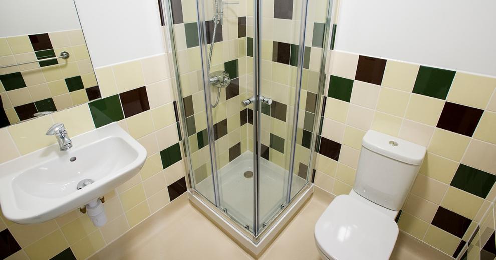 Compact, silver finished single shower cubicle with white toilet and sink in a black and beige tiled bathroom.