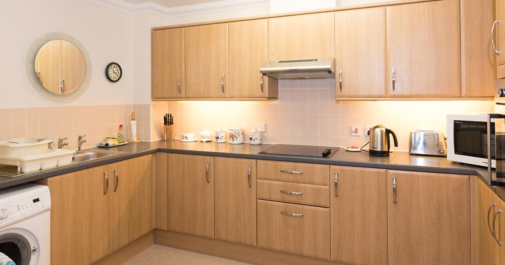 A spacious neutral kitchen featuring plenty of wall mounted cabinetry and draws. With a fitted ceramic hob centred on the worktop. A wall mounted oven is located on the right-hand side and a new washing machine on the left.