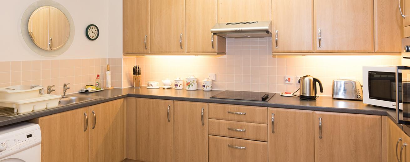 A spacious neutral kitchen featuring plenty of wall mounted cabinetry and draws. With a fitted ceramic hob centred on the worktop. A wall mounted oven is located on the right-hand side and a new washing machine on the left.