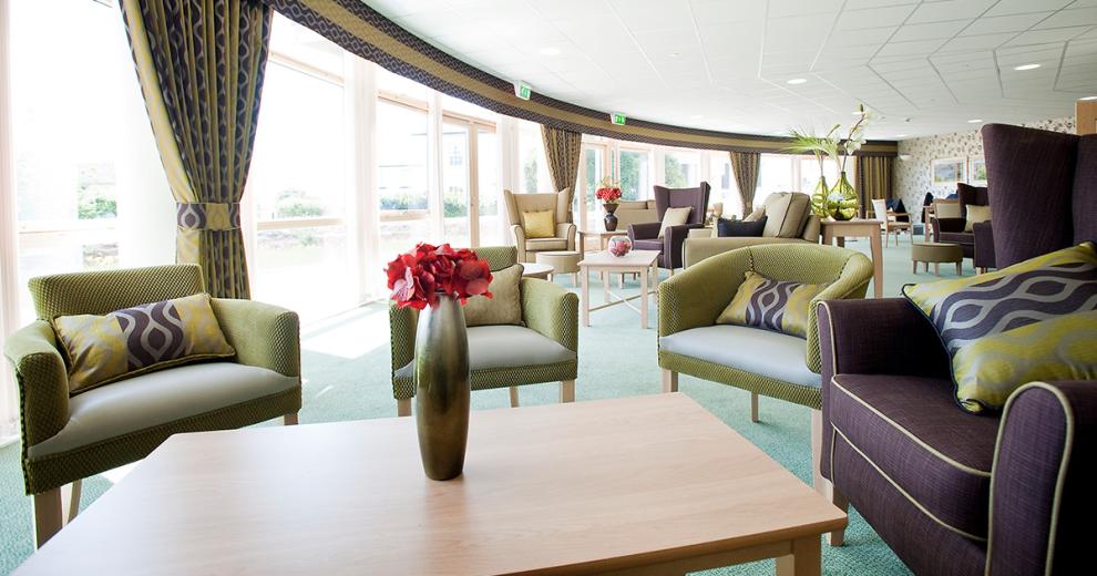 The curved external façade of the building covered in doors and windows allows an abundance of natural light into the seating area. The mix of chairs situated around the room in a mixture of fabric and leather in lime green, purple and cream. All with wood rectangular coffee tables.