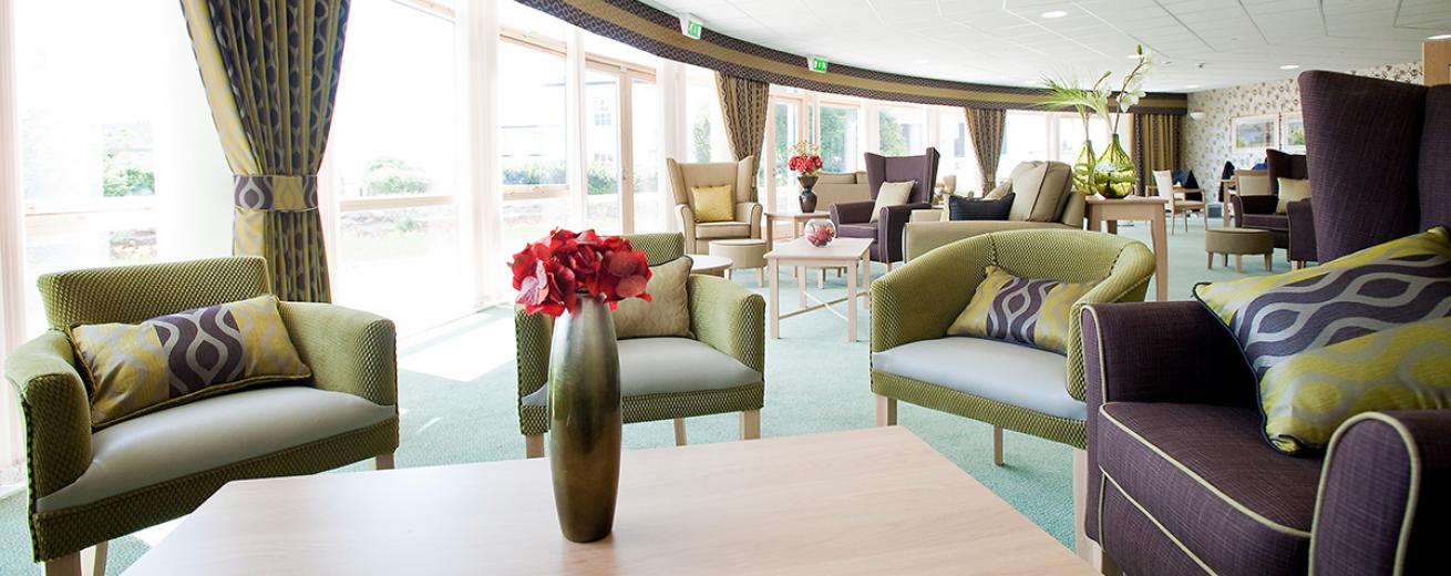 The curved external façade of the building covered in doors and windows allows an abundance of natural light into the seating area. The mix of chairs situated around the room in a mixture of fabric and leather in lime green, purple and cream. All with wood rectangular coffee tables.