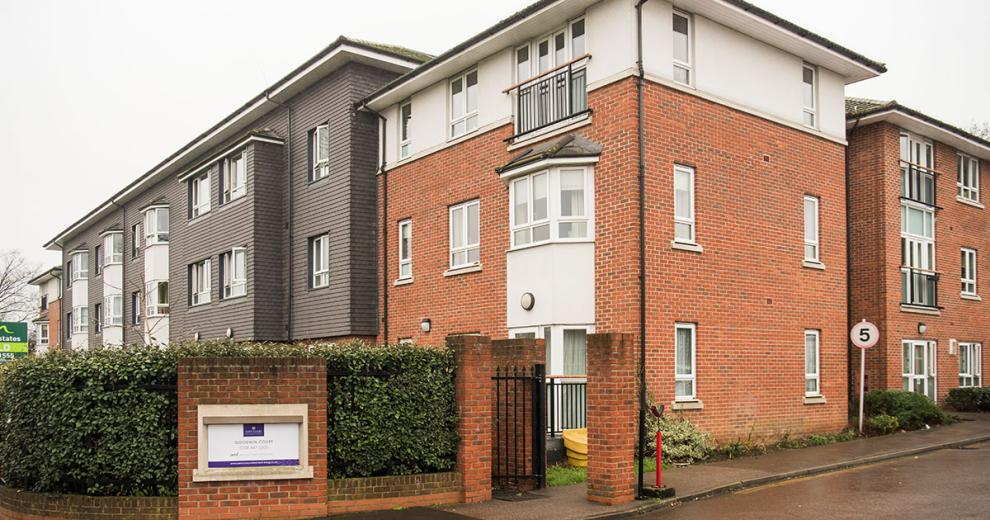 The newly built brick, three storey retirement community. With a large hedge wrapping the front of the property for privacy, an iron gate for pedestrians and a speed restricted driveway.